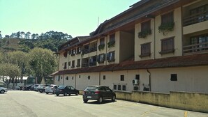 A multi-story building with balconies, parked cars, and a clear sky. - Apartamento dois quartos Capivarí (Campos do Jordão)