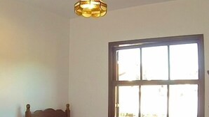 A bedroom with a wooden bed, a bedside table, a window, and a hanging light fixture. - Apartamento dois quartos Capivarí (Campos do Jordão)