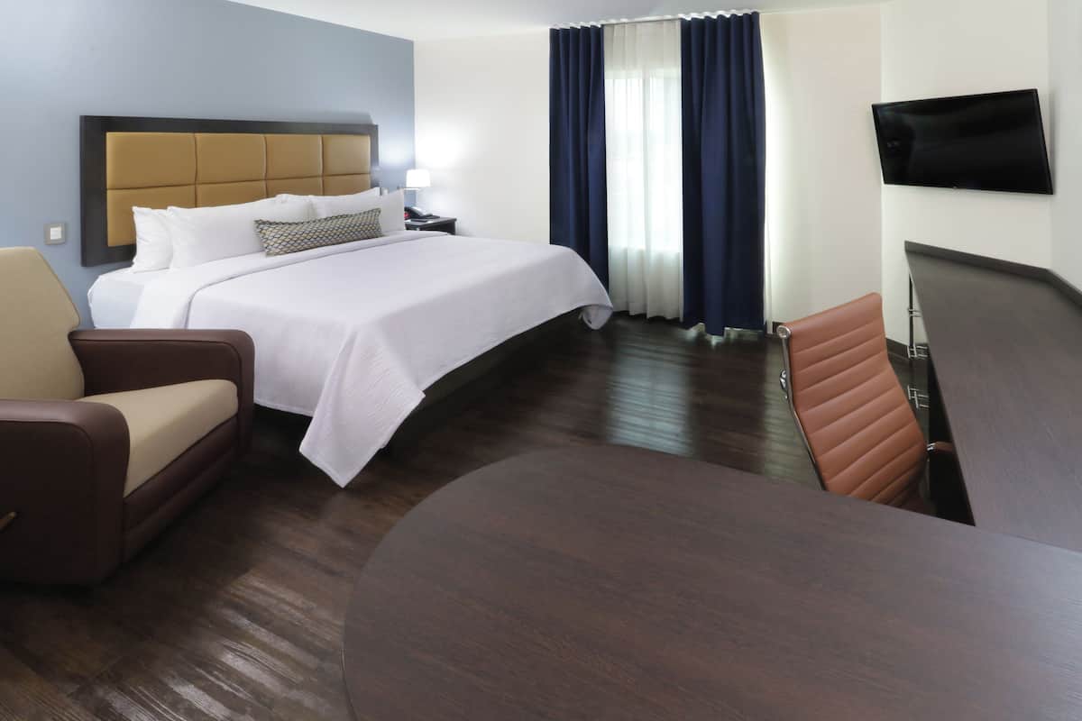 Une chambre d’hôtel avec un grand lit, un canapé, une table à manger, une télévision et une fenêtre avec des rideaux.