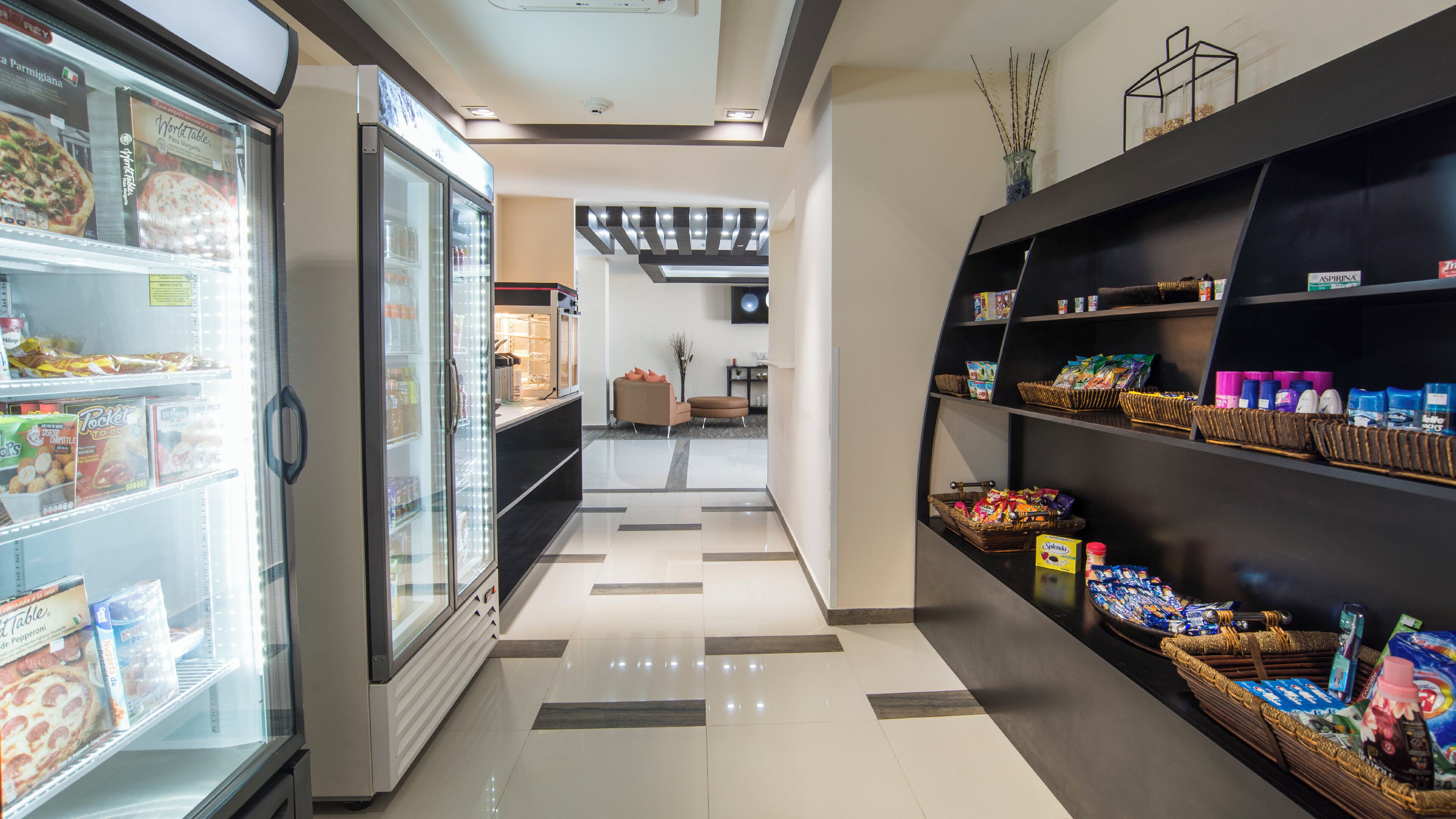 A clean, well-lit corridor with a refrigerated display case on the left and shelves stocked with snacks on the right.