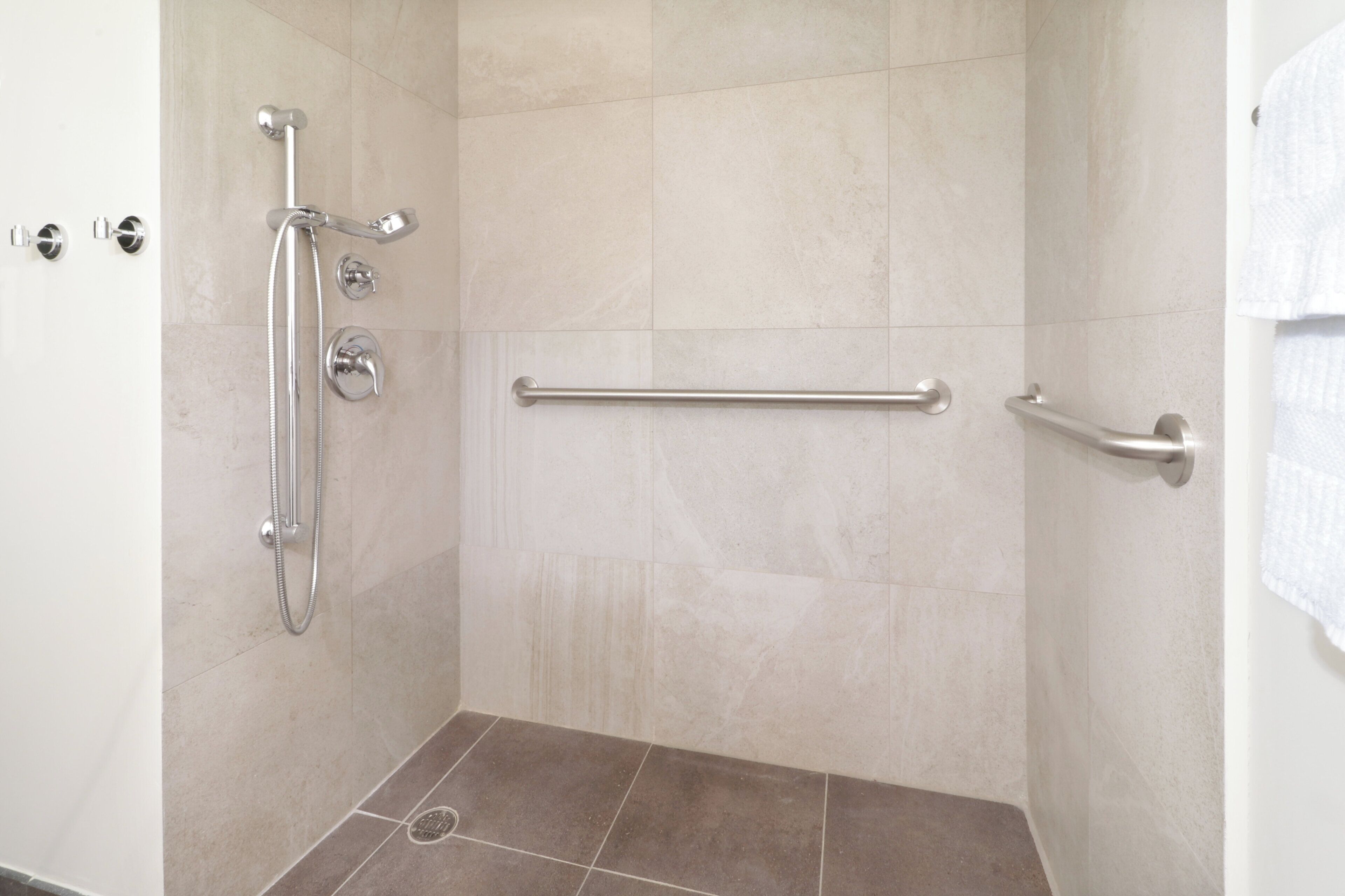 A shower area with a grab bar, a handheld showerhead, and a wall-mounted faucet.