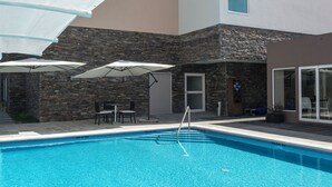 Une piscine avec un mur en pierre en arrière-plan, des sièges extérieurs et des parasols.