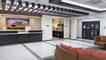 A modern reception area with a receptionist, a large wall mural, a kitchen area, and seating.