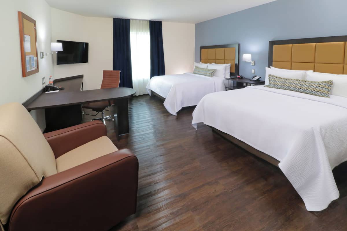 Une chambre d’hôtel équipée d’un bureau, de deux lits, d’une télévision et d’une chaise.
