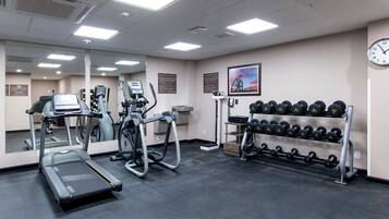 Un gimnasio con cintas de correr, elípticas y un estante con mancuernas.