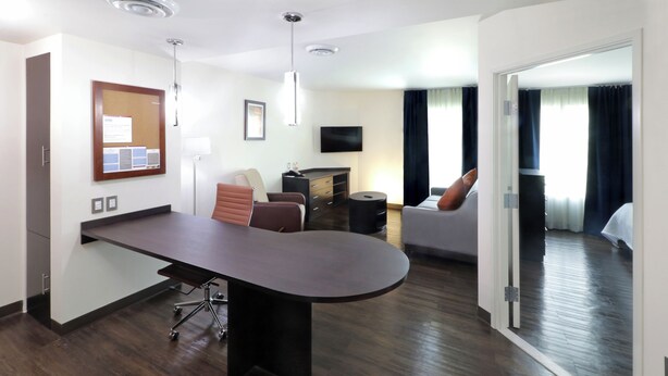 A modern hotel room with a large desk, a flat-screen TV, a fireplace, and a sofa.
