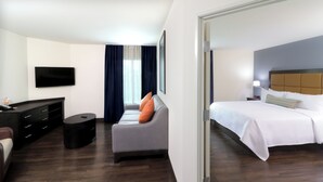 A hotel room with a bed, a sofa, a TV, a desk, and a small table.