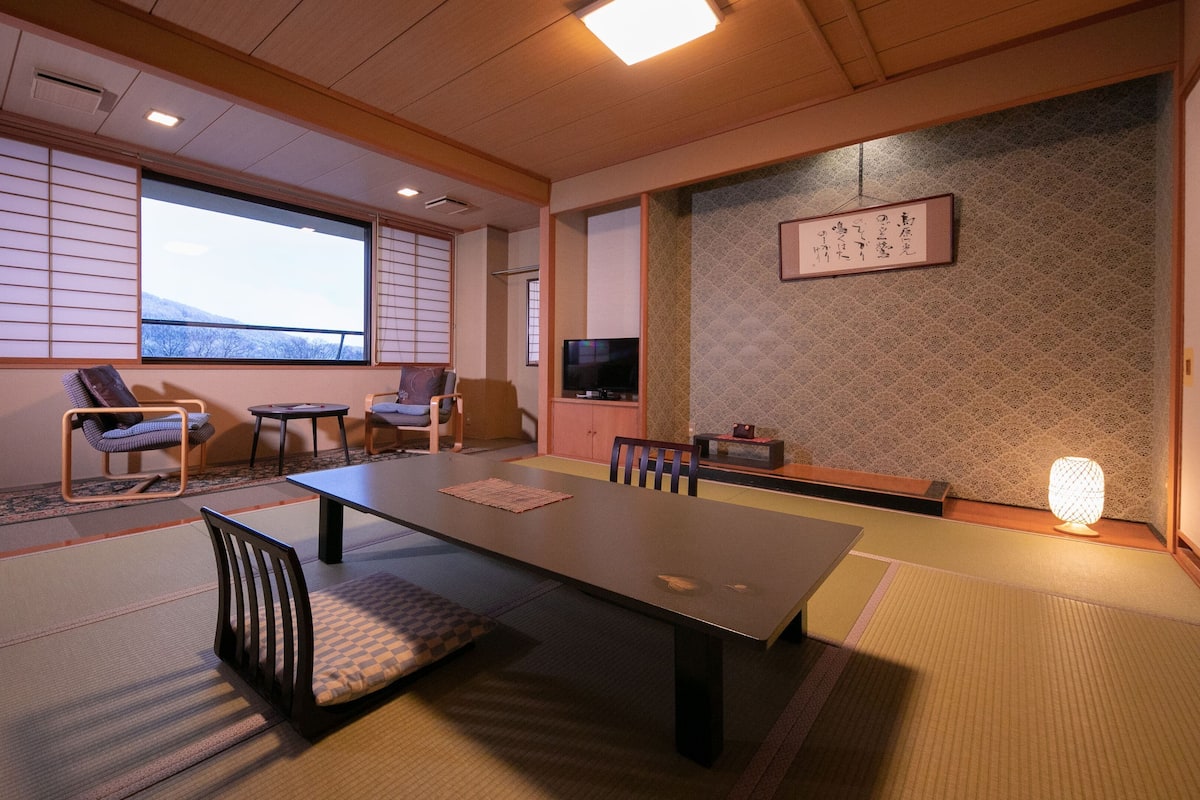 Ein traditioneller japanischer Raum mit Tatami-Boden, einem niedrigen Tisch und zwei Stühlen.