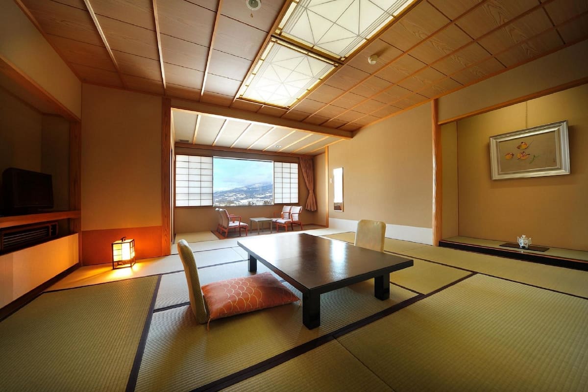 A traditional Japanese room with tatami flooring, a low table, and a view of the city through large windows.
