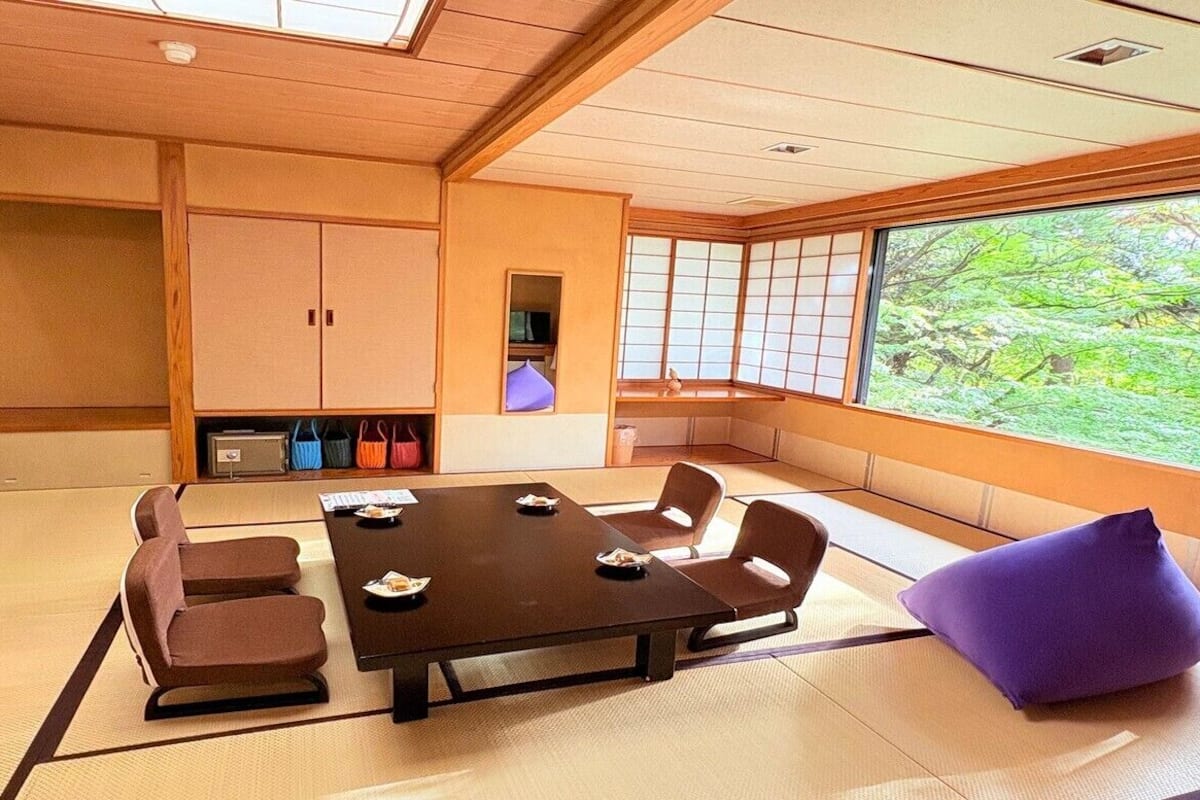 A tatami mat room with a low table, cushions, and a view of greenery.