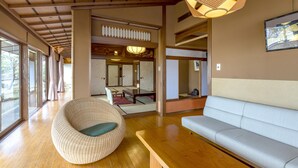 A traditional Japanese-style room with tatami flooring, a low wooden table, a cushioned seating area, and a large window providing natural light. - Senkeien Tsukioka Hotel (Kaminoyama)