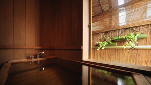 A wooden interior with a large bathtub, bamboo wall, and a small window with plants. - Senkeien Tsukioka Hotel (Kaminoyama)