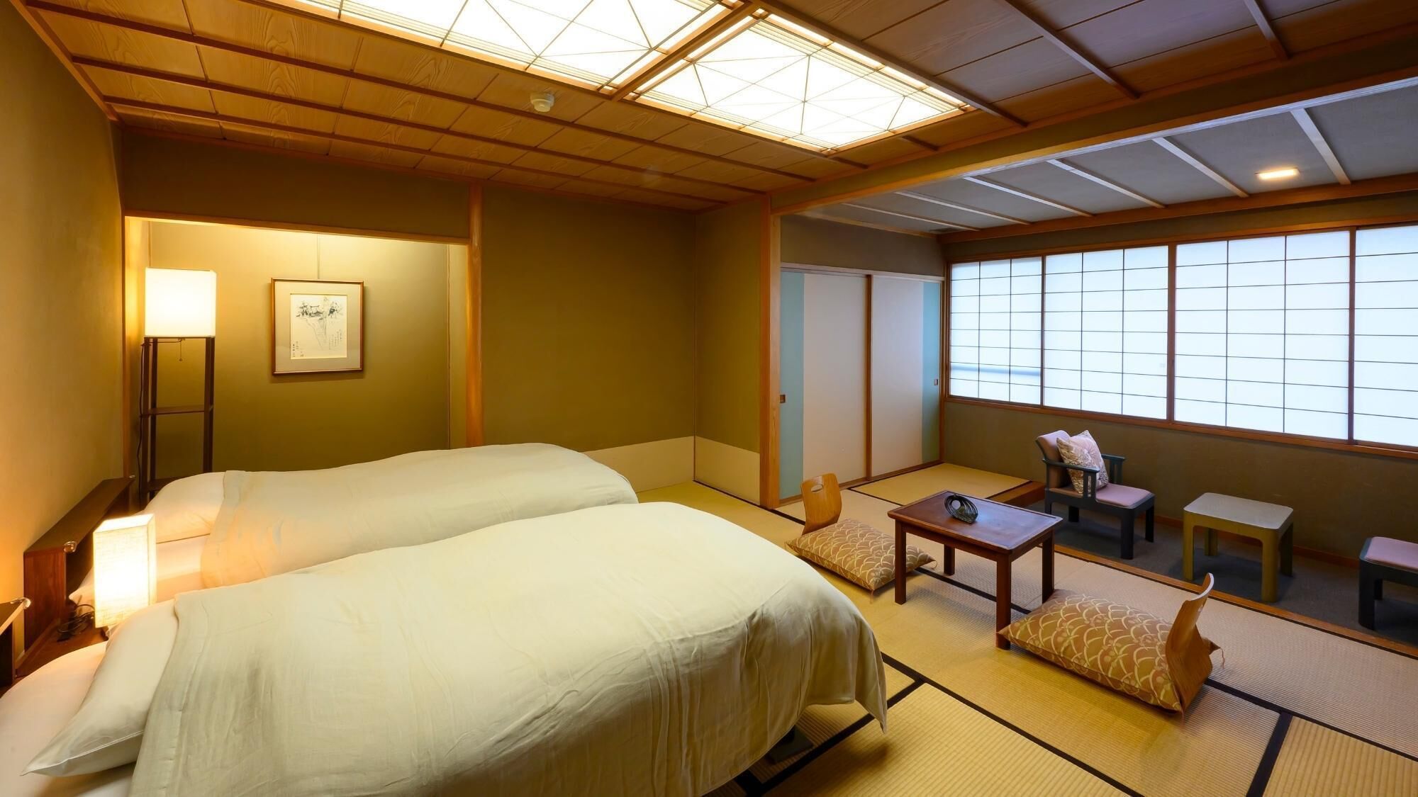 Habitación de hotel con dos camas, una zona de estar con una mesa y sillas, y un ventanal grande.
