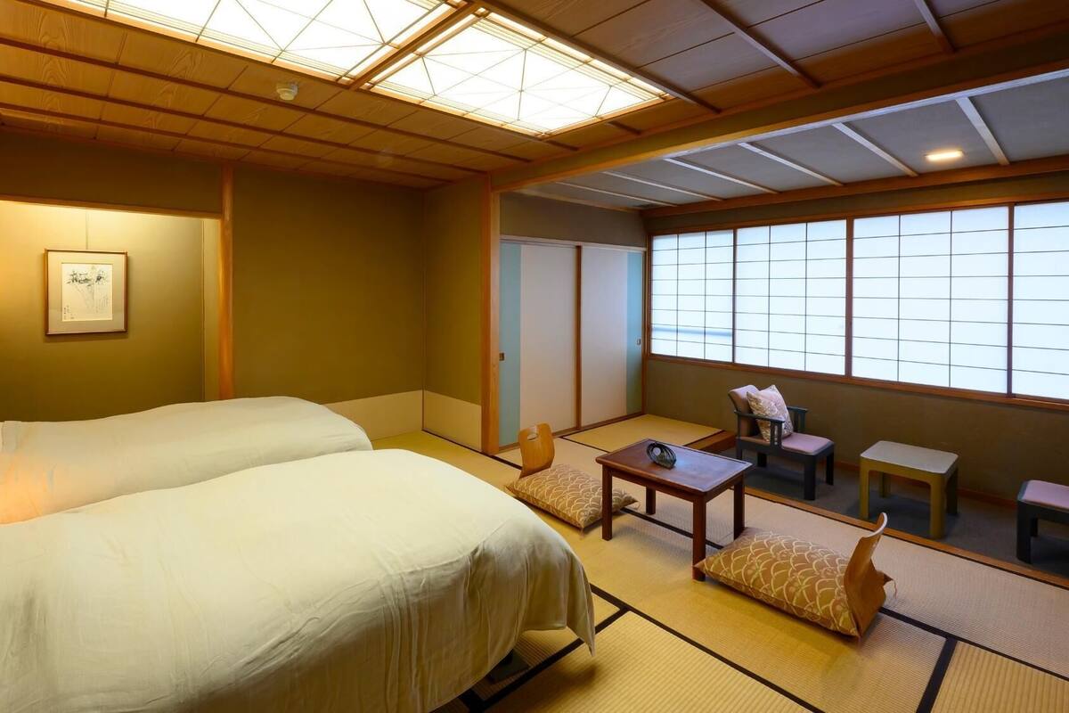 A hotel room with two beds, a sitting area with a table and chairs, and a large window.