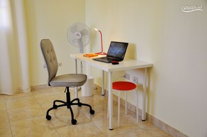 A workspace with a laptop, a chair, a desk, a fan, and a stool.