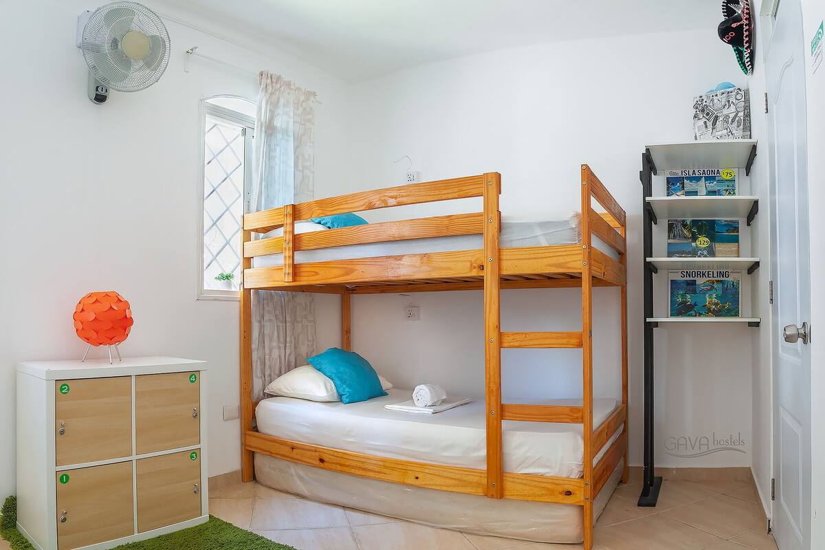 Un lit superposé avec une étagère au-dessus, une petite armoire avec des tiroirs et un tapis vert sur le sol.