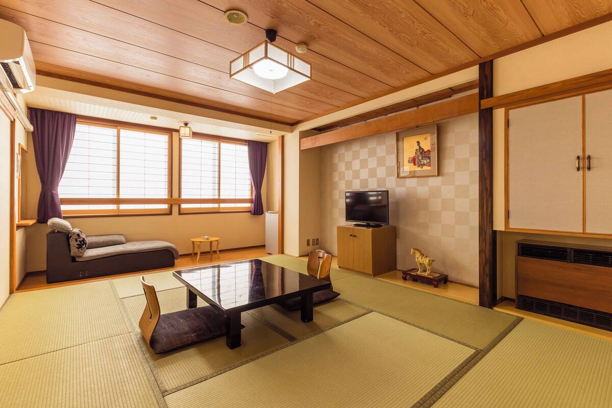 Une pièce de style japonais traditionnel, avec un sol recouvert de tatamis, une table basse, un canapé, un téléviseur et un meuble.