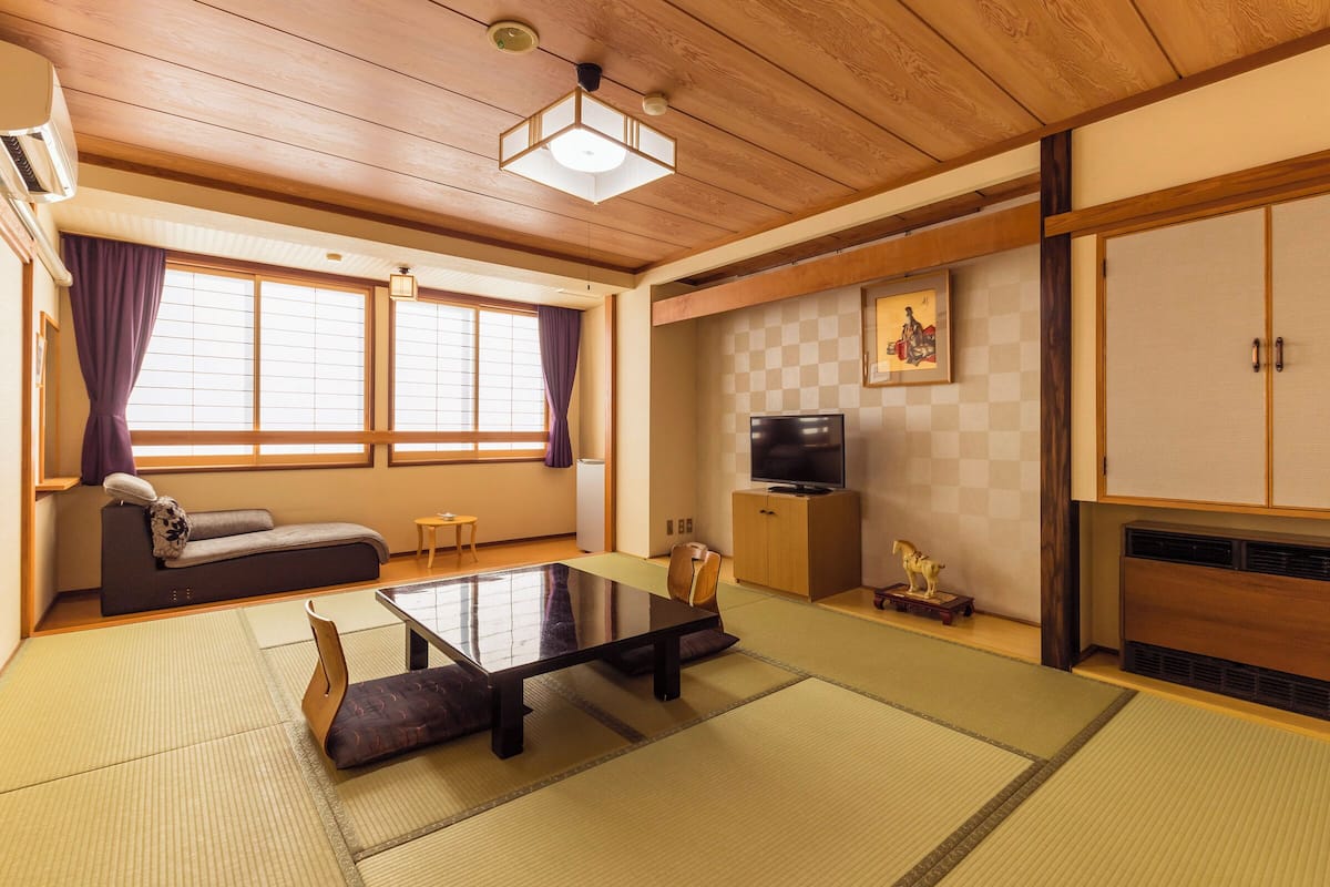 Una habitación japonesa tradicional con suelo de tatami, una mesa baja, un sofá, un televisor y un armario.
