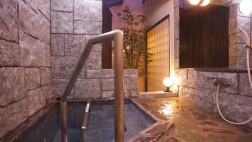A stone-walled hot tub area with a metal ladder, a wooden door, and a mirror reflecting the room.