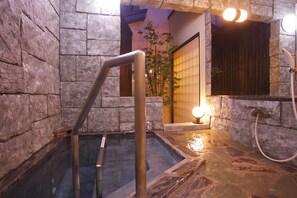 A stone-walled hot tub area with a metal ladder, a wooden door, and a mirror reflecting the room. - Arimakan (Kaminoyama)