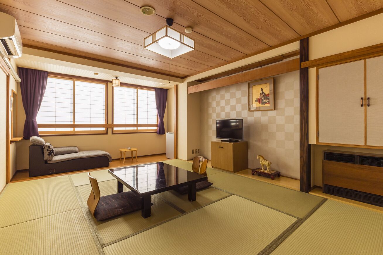 Una habitación japonesa tradicional con suelo de tatami, una mesa baja, un sofá, un televisor y un armario.