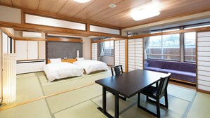 A traditional Japanese room with tatami flooring, a low table with chairs, a bed with white bedding, and a view of the outside through large windows. - Arimakan (Kaminoyama)