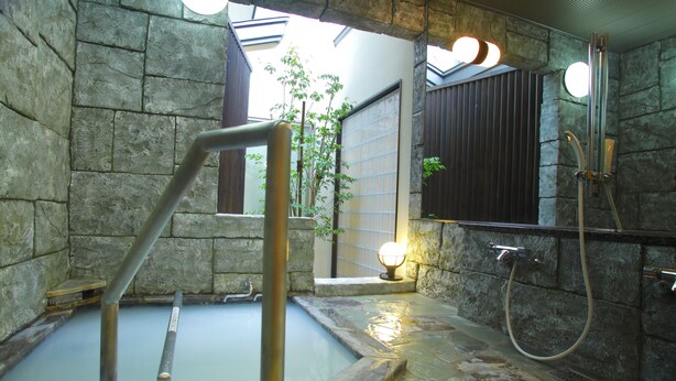 A stone-walled bathroom with a hot spring, a wooden bench, a mirror, and a towel rack. - Arimakan (Kaminoyama)