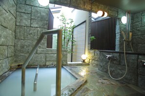 A stone-walled bathroom with a hot spring, a wooden bench, a mirror, and a towel rack. - Arimakan (Kaminoyama)