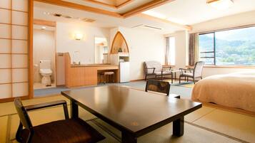 A hotel room with a bed, a dining table with chairs, a small kitchen area, and a view of the outdoors.