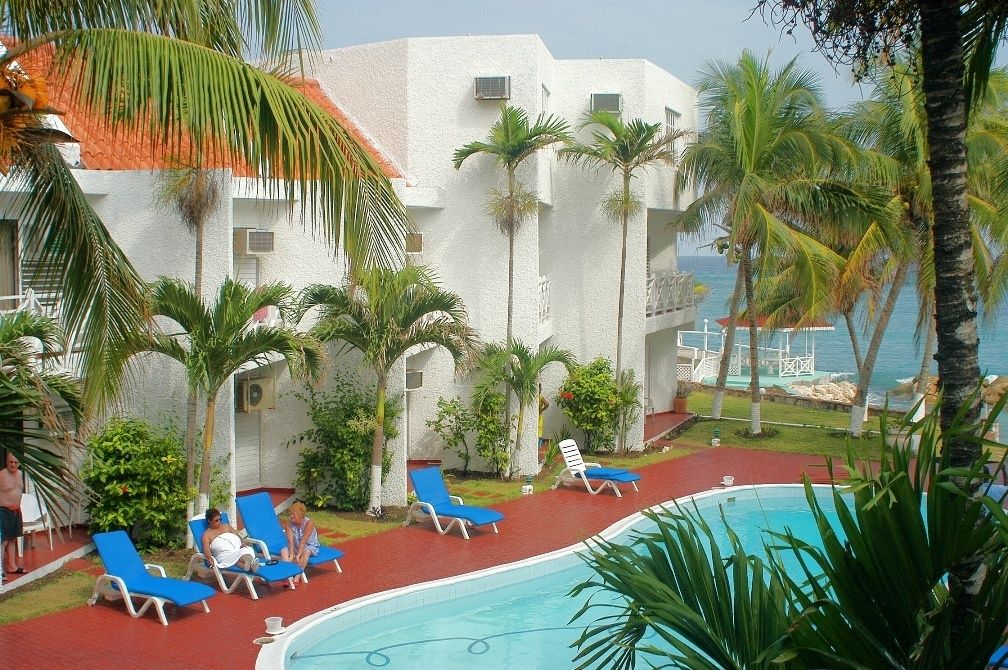 A poolside area with lounge chairs, palm trees, and a view of the ocean.