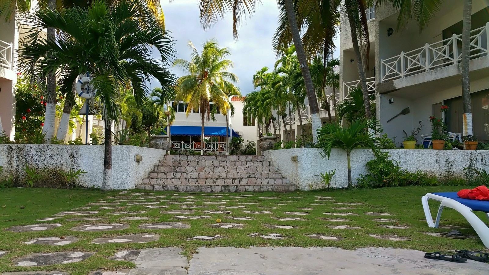 A courtyard with a stone pathway leading to a building with a blue awning.