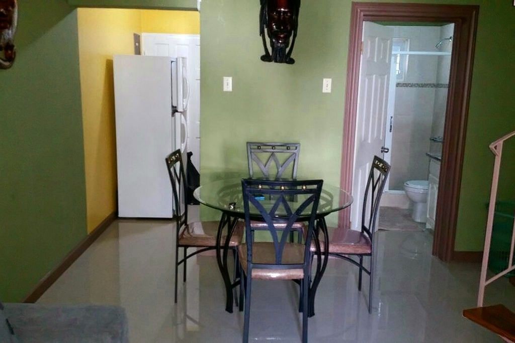A dining area with a glass table and metal chairs, a white refrigerator, and a bathroom visible through an open door.