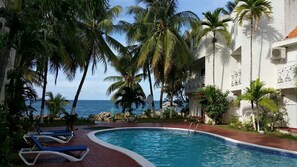 A pool area with lounge chairs, palm trees, and a view of the ocean. - Ocho Rios Beach Resort at ChrisAnn (Tower Isle)