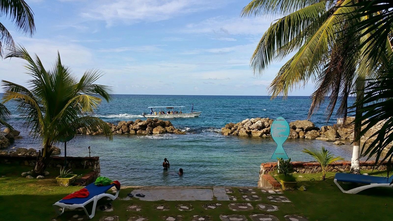 A coastal resort with a pool, palm trees, and a view of the sea.