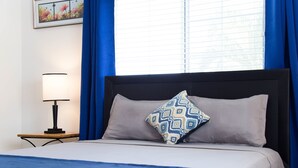 Un letto rifatto con cura, un cuscino decorato, una lampada da comodino e un quadro appeso alla parete.