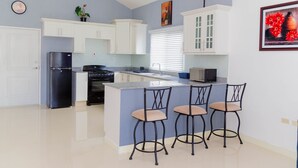 Una cucina moderna con mobili bianchi, un frigorifero nero, un fornello e un forno a microonde. Sono presenti tre sgabelli da bar all'isola.