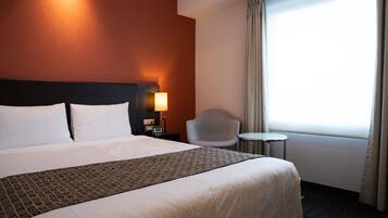 Ein Hotelzimmer mit einem großen Bett, einem Nachttisch mit Lampe, einem Sessel und einem kleinen Tisch.