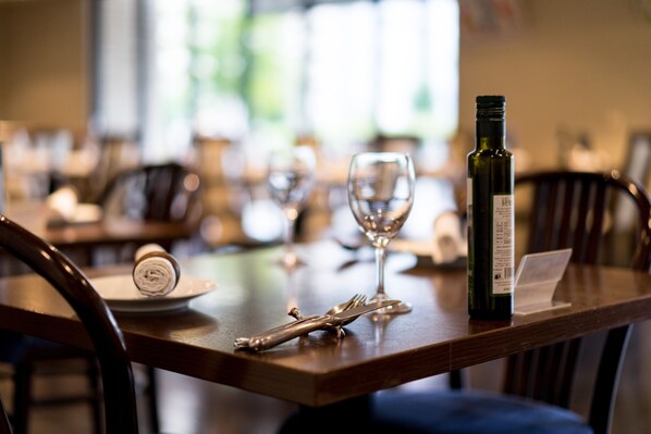 Una mesa de comedor dispuesta con una botella de vino, una copa y cubiertos.