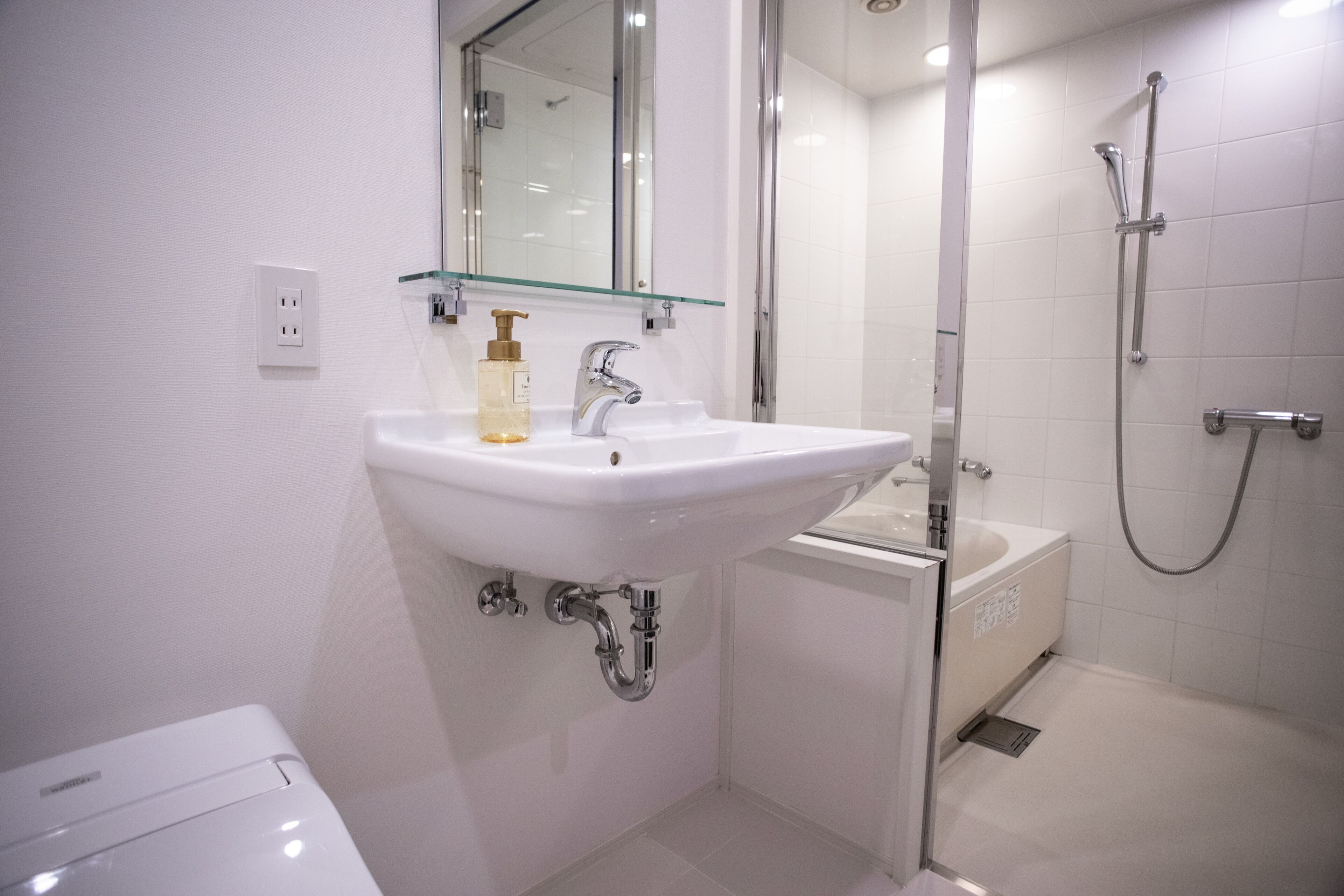 A modern bathroom with a white sink, a glass shelf, a mirror, a shower, and a toilet.