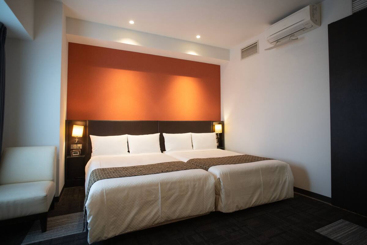 A hotel room with a double bed, two bedside tables, a chair, and a large window.
