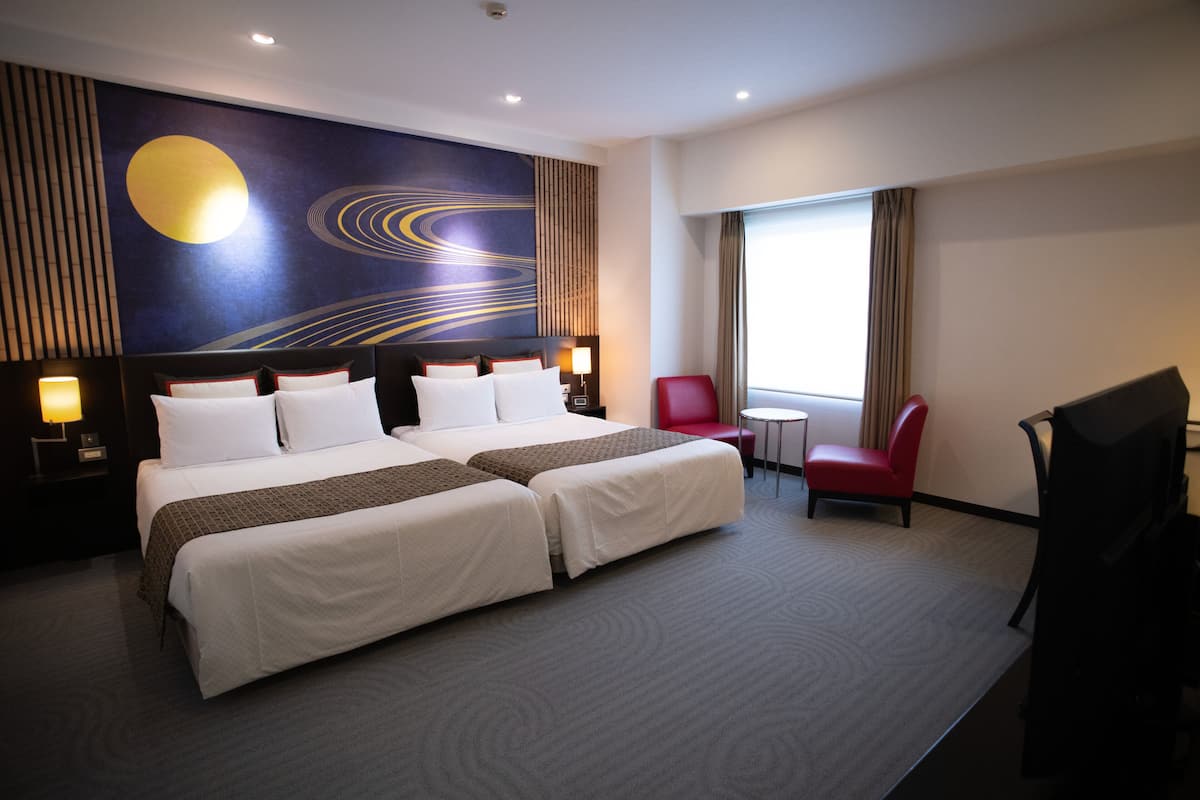 A hotel room with two beds, a red chair, a small table, and a large wall mural.