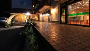 A hotel entrance with a tiled walkway, a curved archway, and a dining area with tables and chairs visible through a glass wall. - Le Vert Zao (Yamagata)