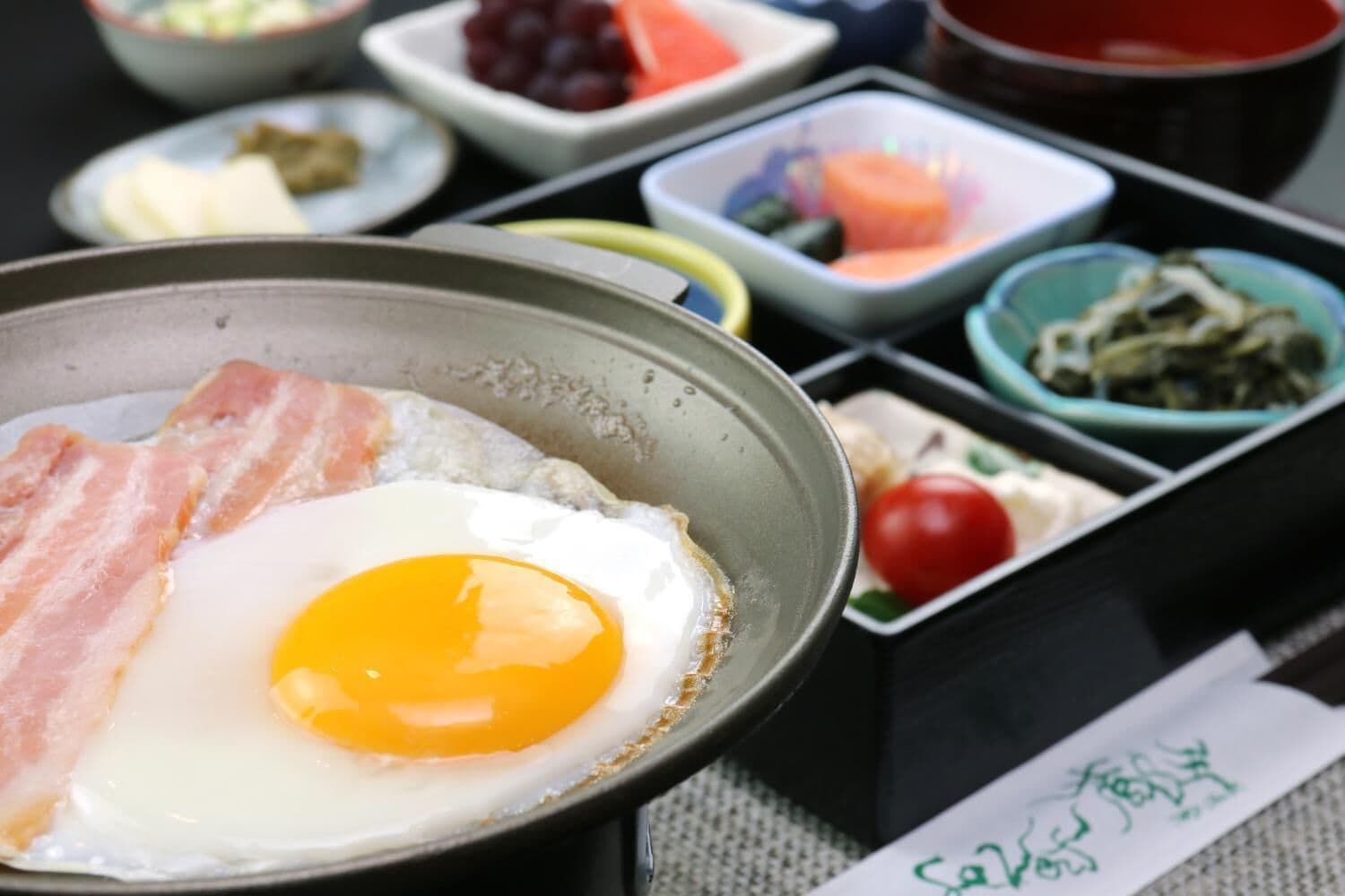 A breakfast tray with a fried egg, bacon, and various side dishes including fruits and vegetables.