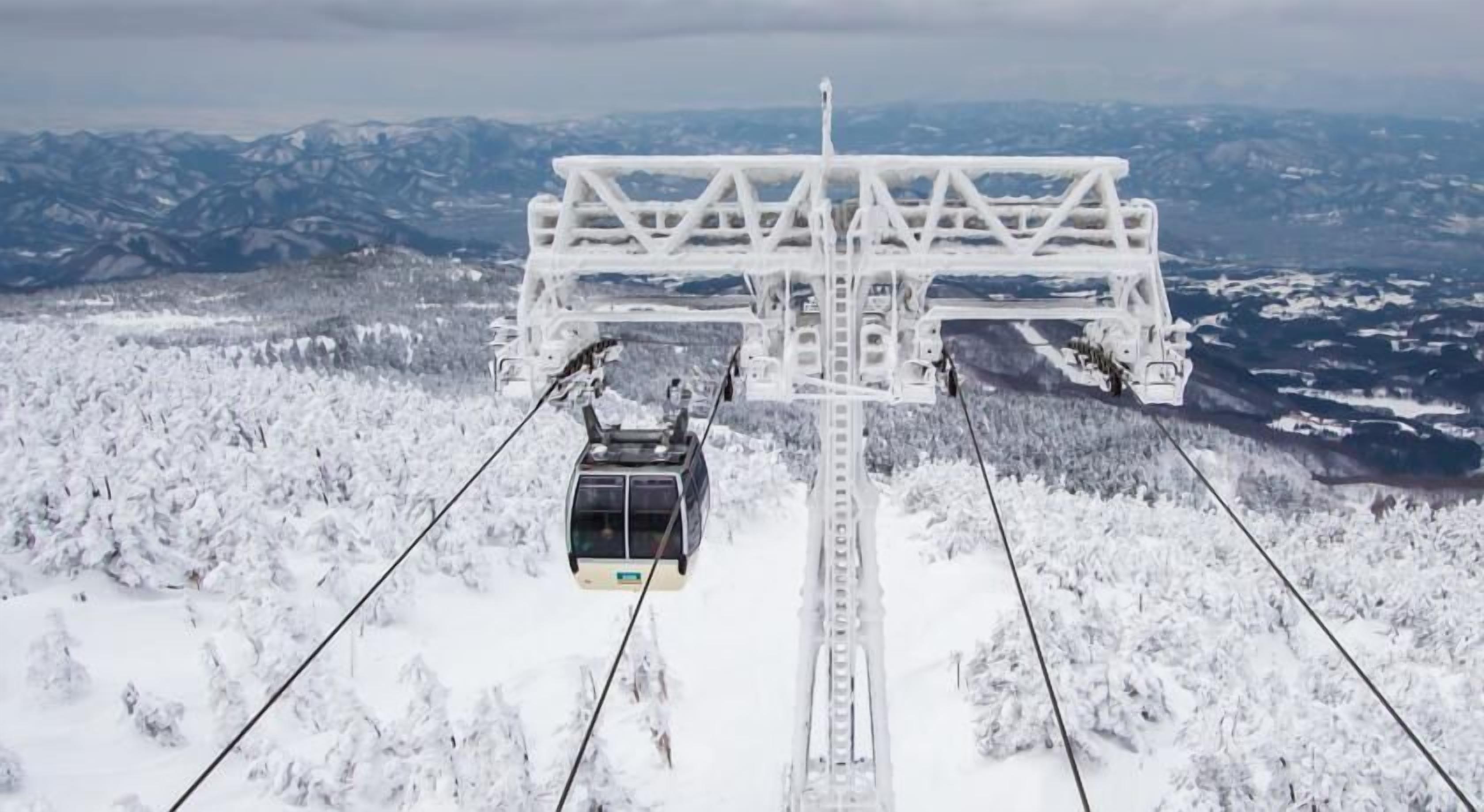 A cable car system with a cable car suspended between two towers, traveling over a snowy landscape with mountains in the background.