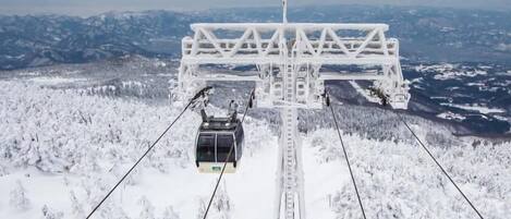 A cable car system with a cable car suspended between two towers, traveling over a snowy landscape with mountains in the background.