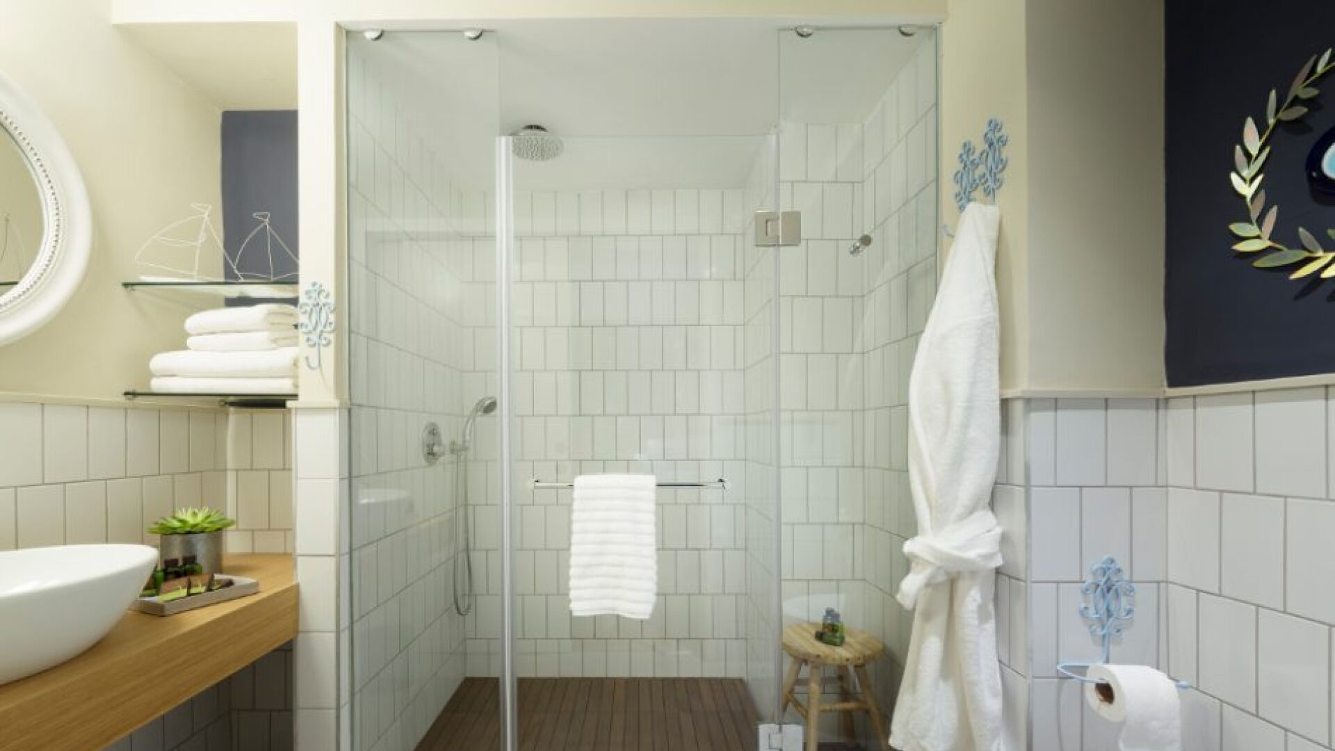 A modern bathroom with a glass-enclosed shower, a wooden vanity with a sink, a small stool, and a toilet paper holder.
