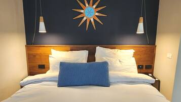 Uma cama com roupa de cama branca, um travesseiro de destaque azul e uma cabeceira de madeira.