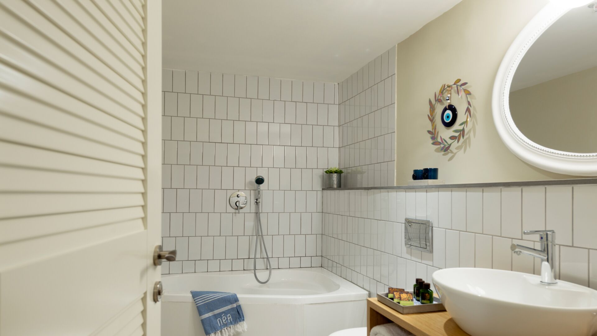 A bathroom with white tiled walls, a bathtub, a sink, and a mirror with a decorative frame.