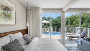 A bedroom with a large bed, a view of a swimming pool, and a balcony with lounge chairs. - Jacob NEA  (Mateh Asher)