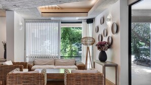 A modern living room with a sofa, wicker chairs, a floor lamp, and a large window with blinds. - Jacob NEA  (Mateh Asher)